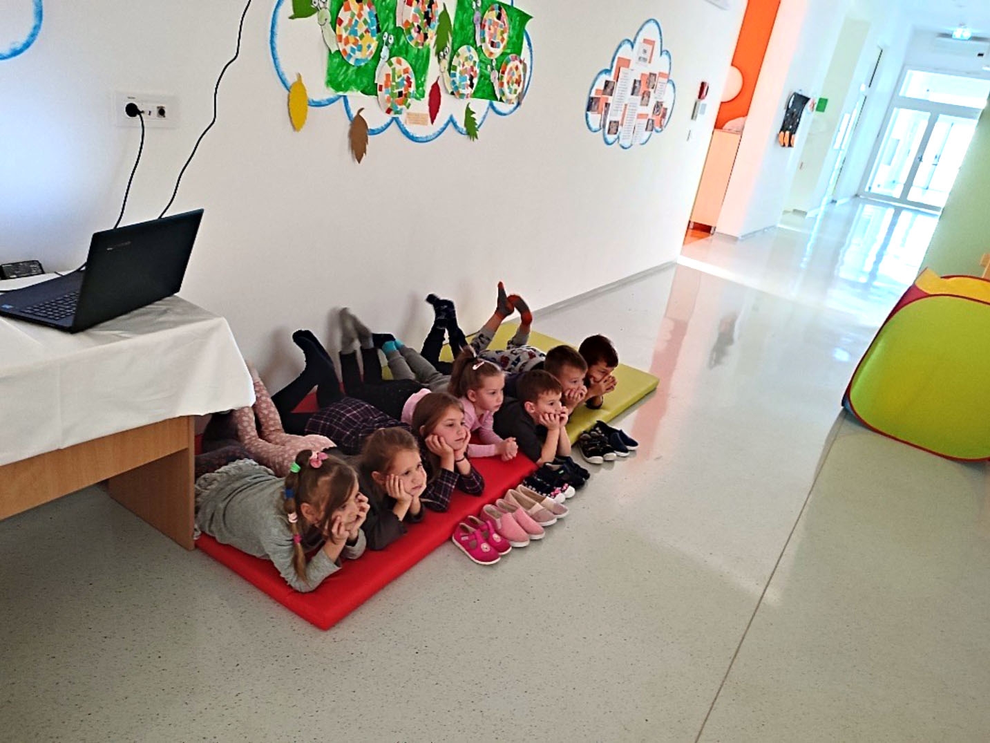 skupina djece leži na strunjači na podu i prati film koji se projicira iz računala.