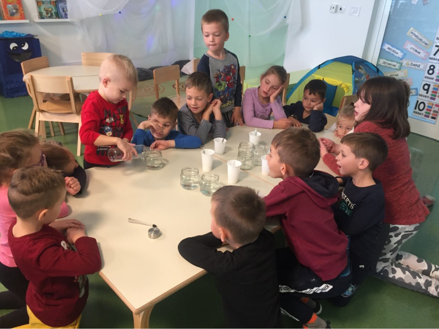 skupina djece sjede za stolom i izvode eksperimente pomoću staklenki